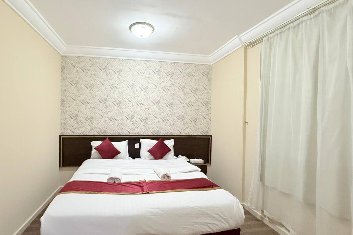 Une chambre d’hôtel avec un grand lit, une tête de lit, une table de chevet et une fenêtre avec des rideaux.