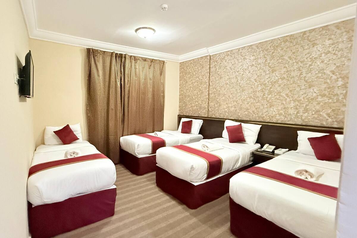 Une chambre d’hôtel avec trois lits, chacun agrémenté de draps blancs et de touches de couleur rouge, une grande fenêtre avec des rideaux et un mur à texture.