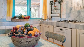 Een keuken met een fruitschaal op tafel, een raam met gordijnen en een fornuis.