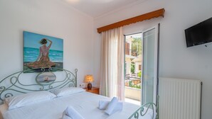 Un dormitorio con cama, un cuadro de una mujer junto al mar, una ventana con cortinas y un televisor montado en la pared.