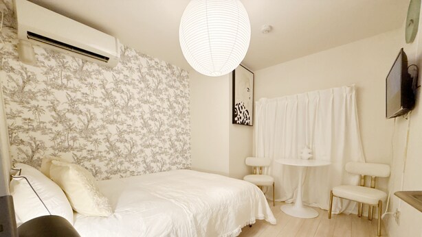 A bedroom with a bed, bedside tables, a desk, a chair, a lamp, a wall-mounted TV, and a ceiling light.