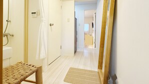 A hallway with a wooden bench, a white door with a towel hanging, and a shower area with a hose.