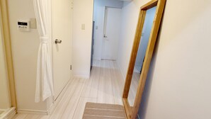 A hallway with a wooden floor, a white door with a towel hanging on it, a wooden-framed mirror, and a light switch on the wall.