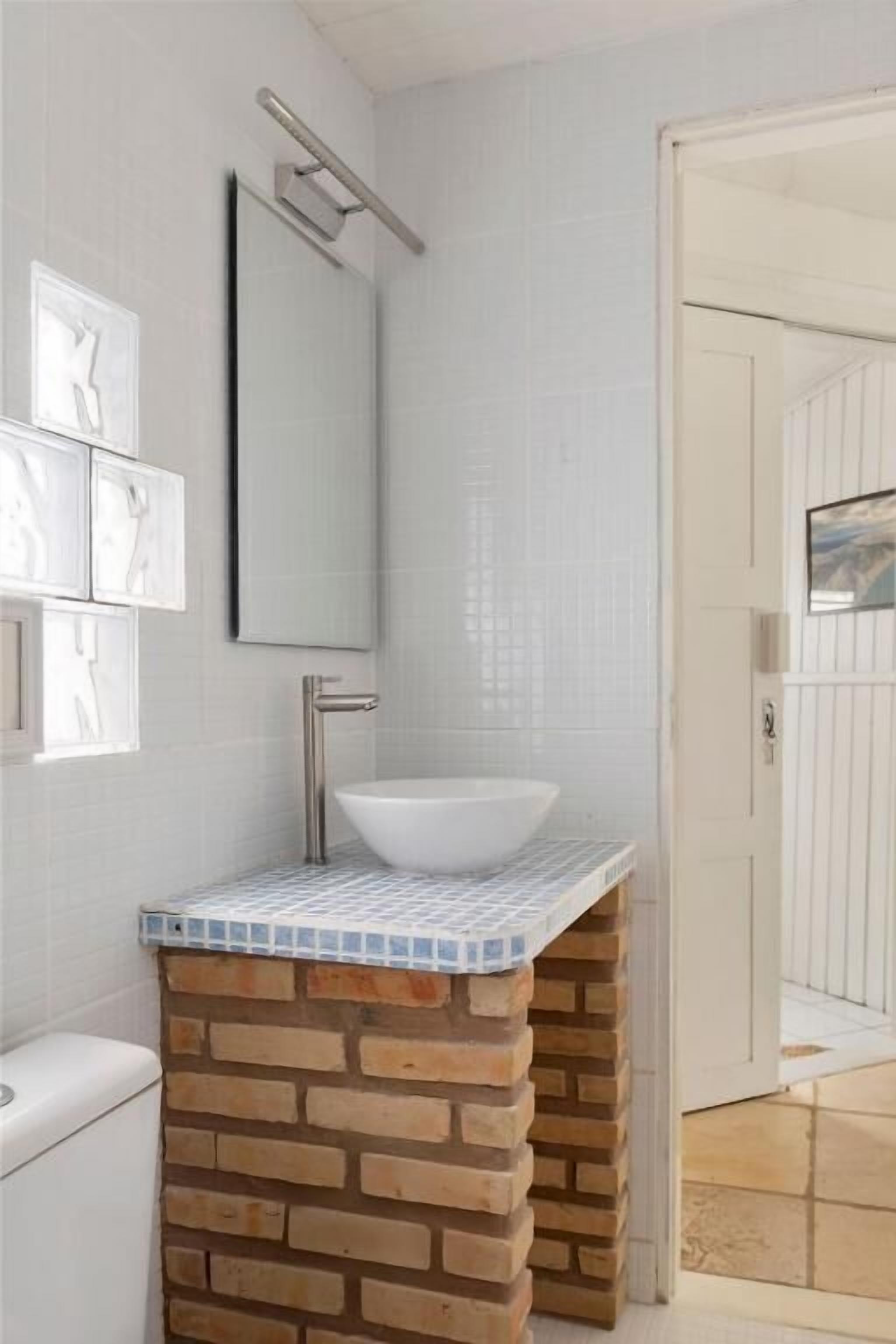 Casa de banho com lavatório branco, espelho e painel de azulejos.