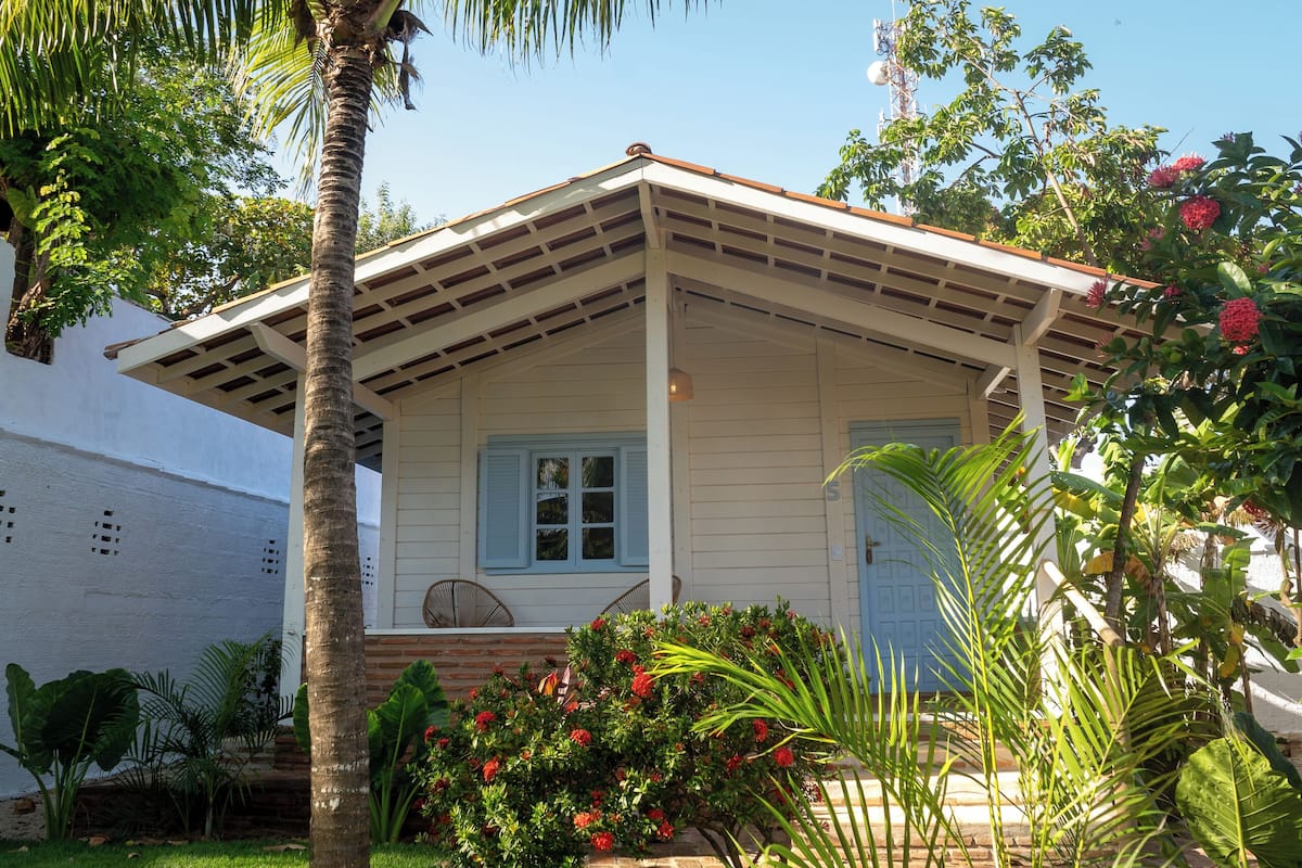 Ein Haus mit einer Veranda, umgeben von einem gepflegten Garten mit Palmen und blühenden Pflanzen.
