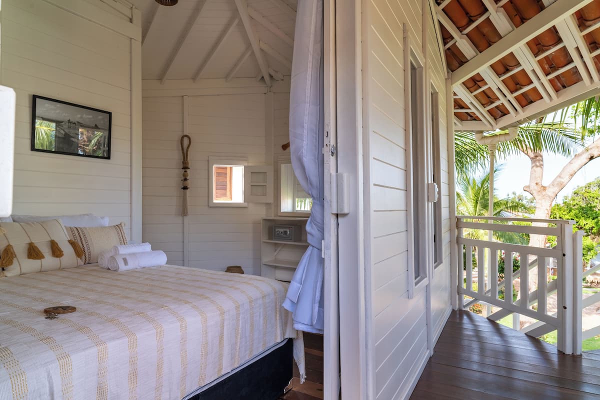 Ein Schlafzimmer mit Bett, Fenster, Tür und Blick ins Freie.