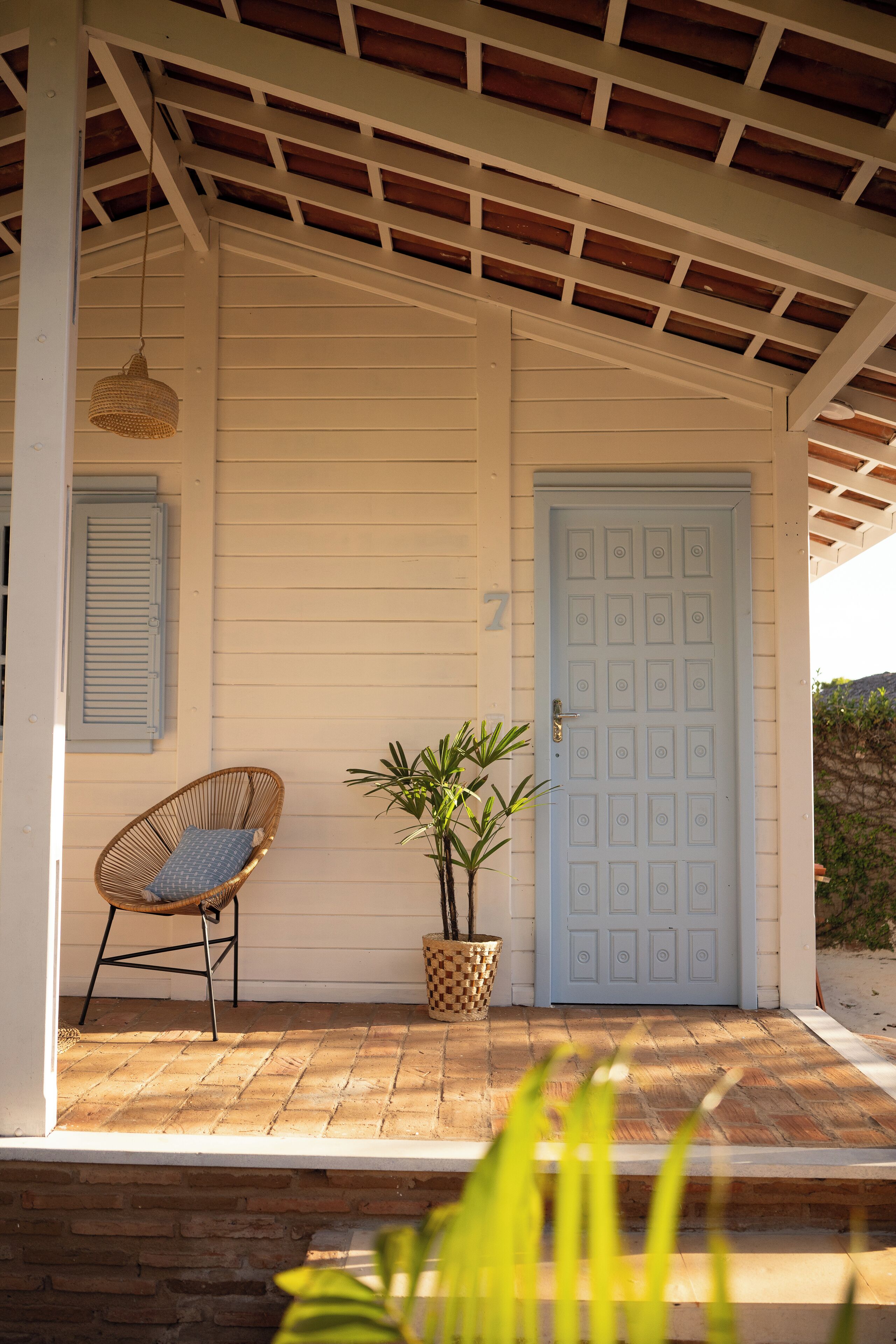 A porch with a wicker chair, a potted plant, and a blue door.