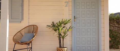 A porch with a wicker chair, a potted plant, and a blue door.