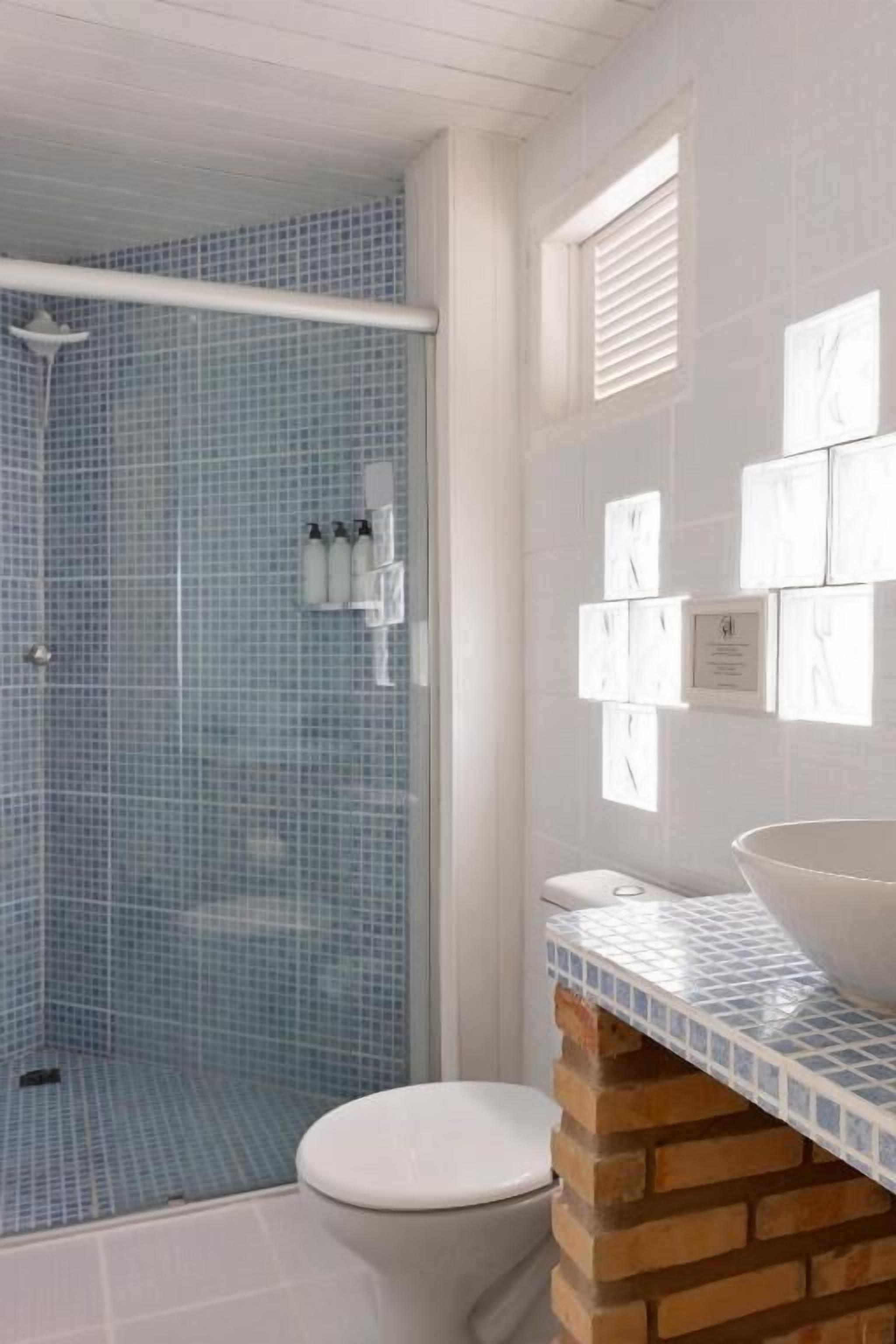 A bathroom with a glass shower enclosure, a white toilet, and a sink with a mosaic tile countertop.