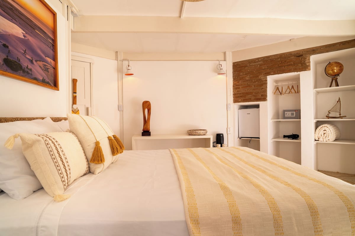 Ein Schlafzimmer mit einem großen Bett, weißen Wänden, einem Holzkopfende, einem Regal mit einem Globus und einem Wandsegment aus Backsteinen.