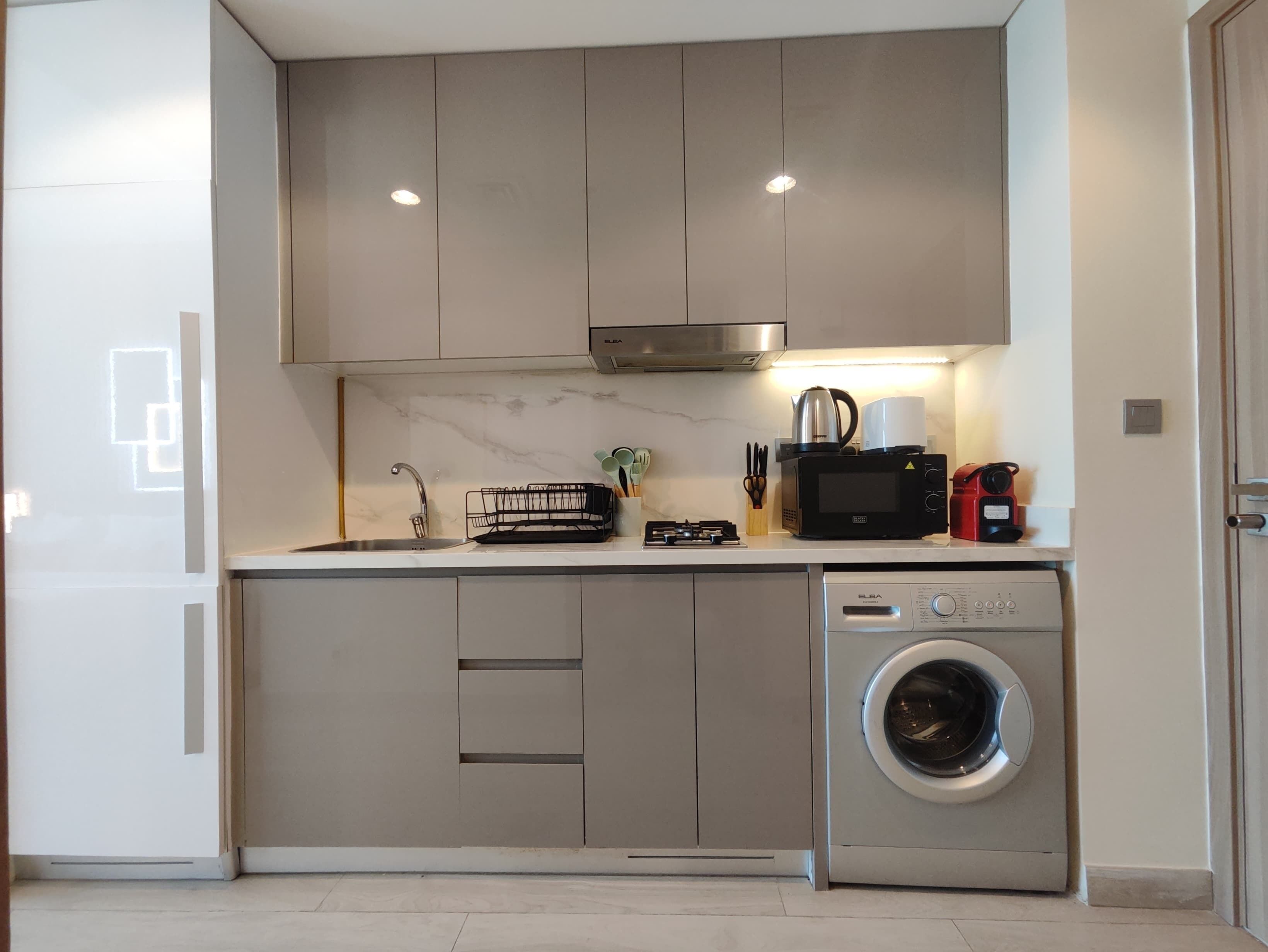 A modern kitchen with a built-in washing machine, a microwave, and a coffee maker.