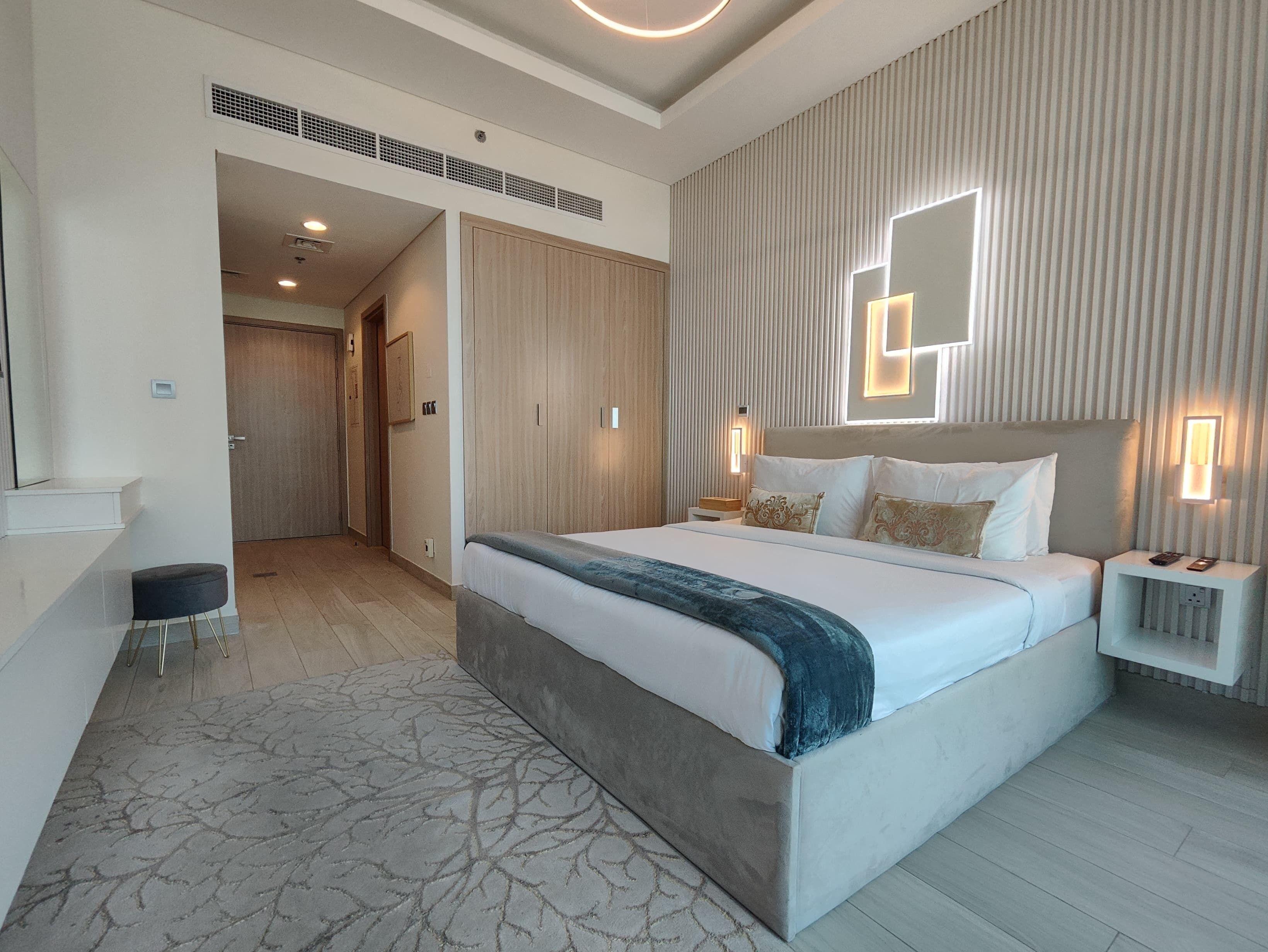 Una habitación de hotel moderna con una cama grande, mesitas de noche, un escritorio y una alfombra estampada.