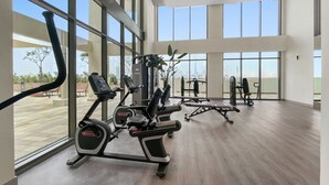A spacious gym with various exercise equipment, large windows, and a view of the outdoors. - Lux BnB Farhad Azizi- Al Jaddaf  (Dubai)