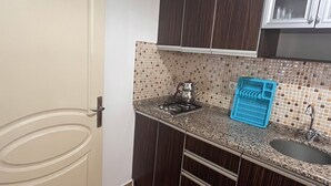 A compact kitchen with dark wood cabinets, a tiled backsplash, a gas stove, and a sink. - İSKELE APART AVŞA  (Marmara)