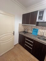 Eine kleine Küche mit dunklen Holzausziehtüren, einer gefliesten Spritzschutzwand, einem Gasherd und einem Spülbecken.