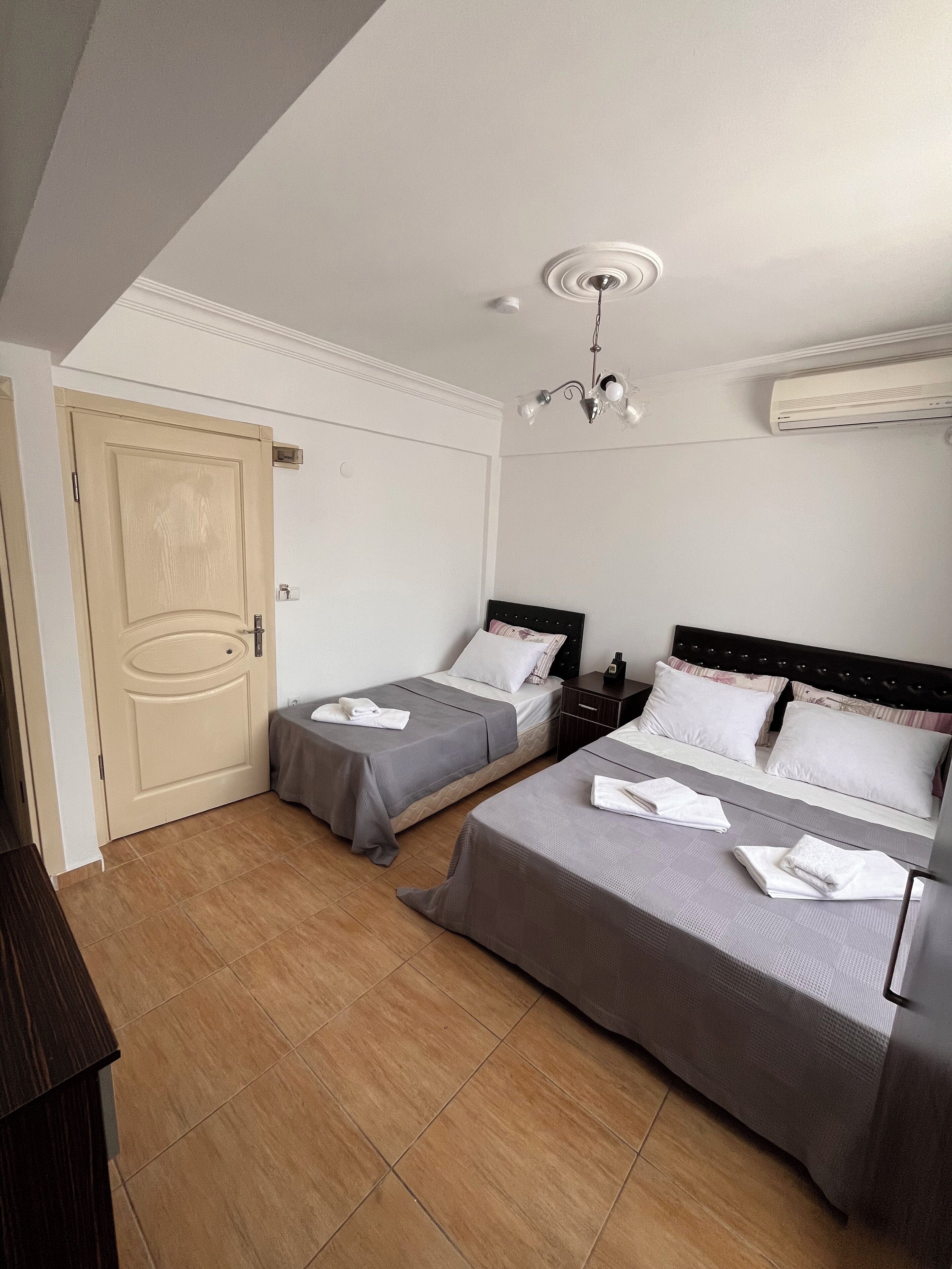A bedroom with two beds, a door, a nightstand, a chandelier, and an air conditioning unit.