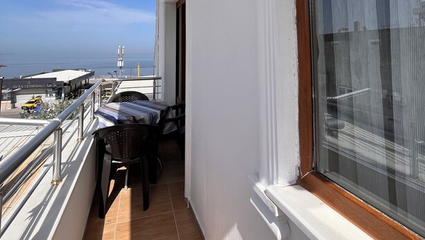 A balcony with a view of the sea, a table, chairs, and a window with a curtain. - İSKELE APART AVŞA  (Marmara)