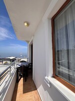 Ein Balkon mit Meerblick, inklusive Tisch, Stühlen und einem Fenster mit Vorhang.