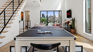 A modern living room with a ping pong table, a black chair, and a staircase. - Ultimate Group Getaway - Twin Lofts - Sleeps 20 (Dallas)