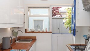 A compact kitchen with white cabinets, a wooden countertop, a window with a view, and a gas stove. - Kenny Cottage (Dawlish)