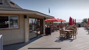 En træterrasse med udendørs siddepladser og røde parasoller, en bygning med et flag, og en klar himmel.