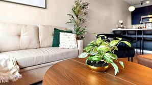 A modern living room with a round wooden coffee table, a beige sofa with a green throw pillow, and a potted plant on the table. - Stylish 1B in DT Minneapolis, Minutes to Minneapolis Convention Center & US Bank (Minneapolis)