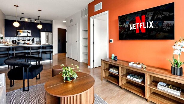 A modern living room with a large TV mounted on an orange wall, a wooden coffee table, and a black sofa. - Stylish 1B in DT Minneapolis, Minutes to Minneapolis Convention Center & US Bank (Minneapolis)