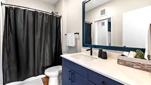 A modern bathroom with a black shower curtain, white toilet, and a large mirror above the sink. - Stylish 1B in DT Minneapolis, Minutes to Minneapolis Convention Center & US Bank (Minneapolis)