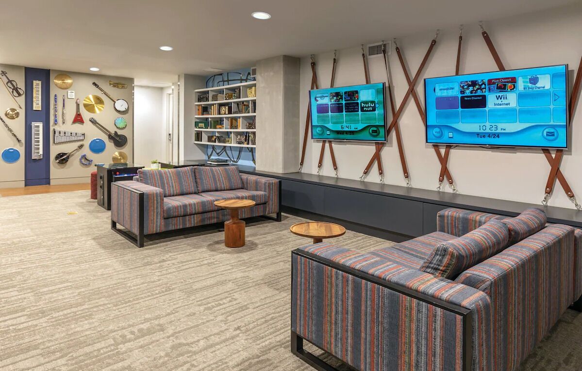 A modern lounge area with striped sofas, a bookshelf, and a large flat-screen TV displaying a schedule.