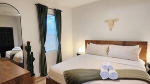 A hotel room with a wooden bed, a ceiling fan, a cactus plant, and a bull skull decoration.