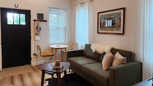 A cozy living room with a wooden ceiling, a ceiling fan, a green sofa with pillows, a coffee table, and a black and white rug.