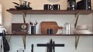A kitchen with a clock, stove, shelves with kitchenware, and a coffee maker.