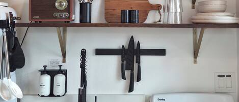 Una cocina con un reloj, estufa, estantes con utensilios de cocina y una cafetera.