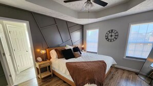 Un dormitorio moderno con una cama, mesitas de noche, un reloj y ventanas amplias.