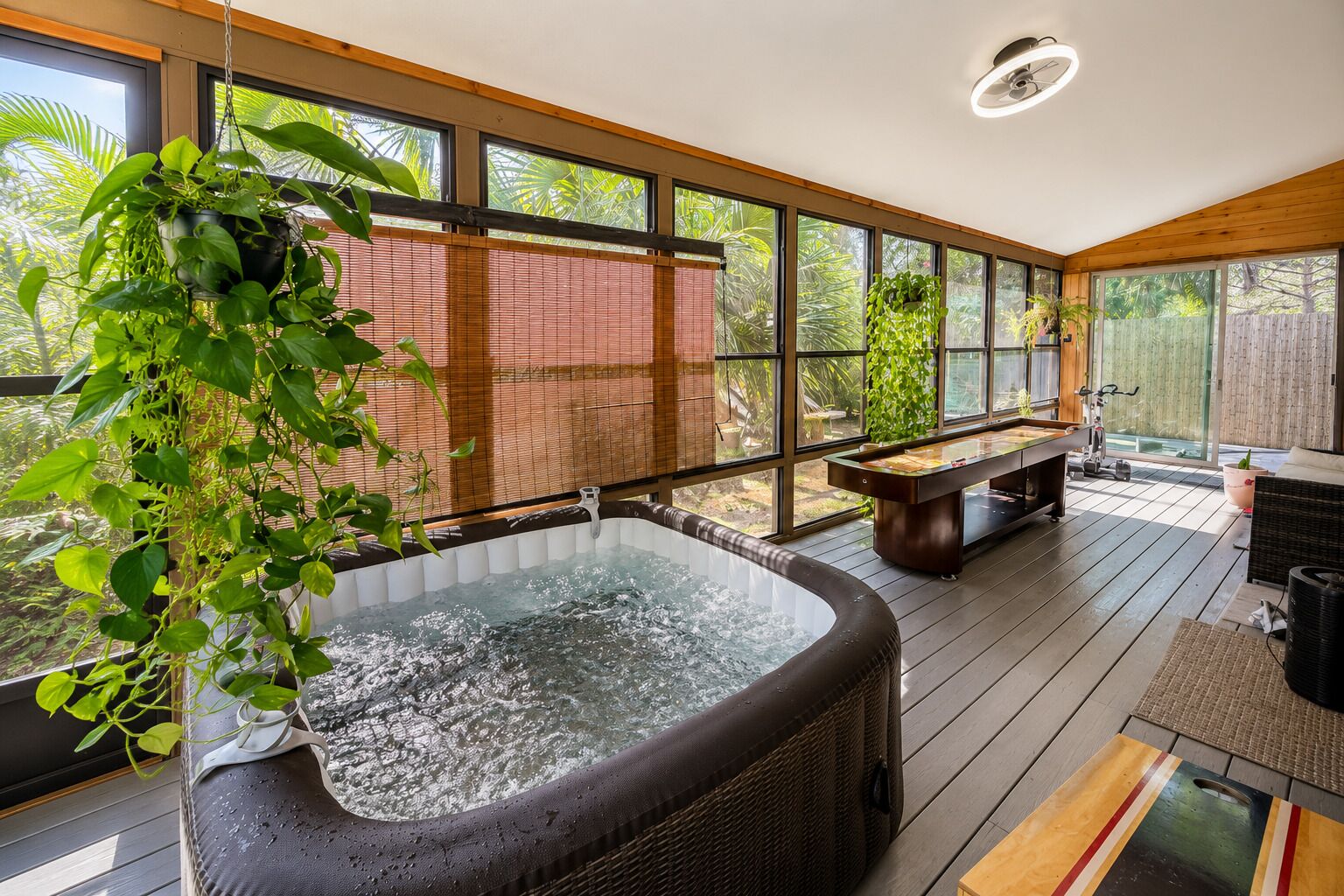 Un jacuzzi en una terraza de madera con ventanas amplias y plantas en macetas.