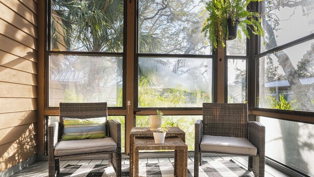 A room with two wicker chairs, a small table with a plant, and a view of trees through large windows. - Waterfront Zen-Dock, Paddleboards, Jacuzzi & Games (St. Augustine)