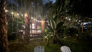 A patio area with two Adirondack chairs, a palm tree, and string lights. - Waterfront Zen-Dock, Paddleboards, Jacuzzi & Games (St. Augustine)