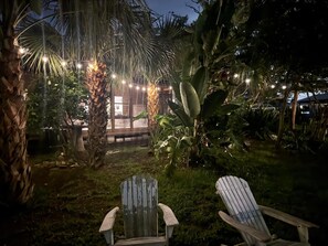 Ein Patio mit zwei Adirondack-Stühlen, einer Palme und Lichterketten.