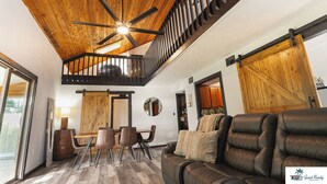 A spacious living area with a high ceiling fan, a dining table with chairs, a leather sofa, and a staircase leading to an upper level. - Waterfront Zen-Dock, Paddleboards, Jacuzzi & Games (St. Augustine)