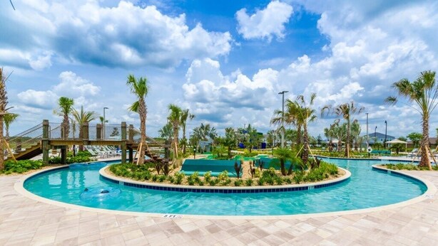 A swimming pool with palm trees and a bridge in the background.