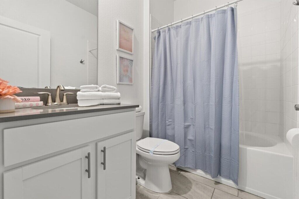 Une salle de bain comprenant des toilettes, un lavabo avec un miroir, un porte-serviettes avec des serviettes pliées et un rideau de douche.