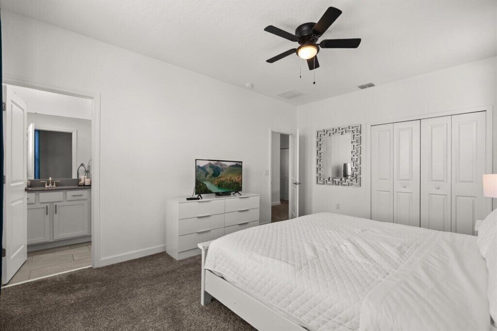 A bedroom with a bed, a ceiling fan, a TV, a dresser, and a wardrobe.