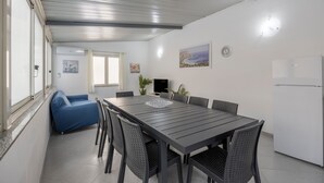 Una zona de menjador moderna amb una taula llarga, cadires, un sofà blau i un frigorífic blanc.
