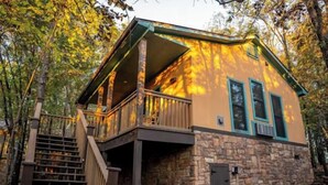 Une cabane avec des fondations en pierre, une terrasse en bois et un porche couvert.