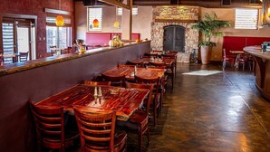 L’intérieur d’un restaurant avec des tables et des chaises en bois, une cheminée en pierre et une grande plante en pot.