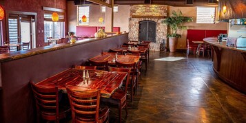 Un interior de restaurante con mesas y sillas de madera, una chimenea de piedra y una planta grande en maceta.