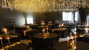 Une salle de banquet avec des tables rondes, chacune décorée de bougies et de verdure.