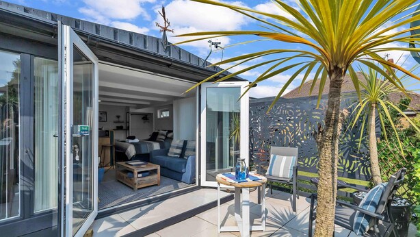 A modern house with a glass door leading to a living area with a sofa and coffee table. - Garden Room With Parking | By My Getaways (Lancing)