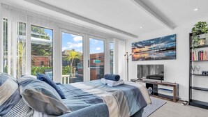 A modern hotel room with a large bed, a TV, and a bookshelf. - Garden Room With Parking | By My Getaways (Lancing)