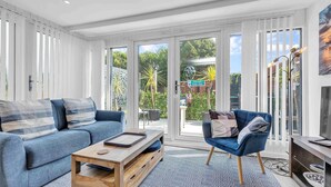 A modern living room with a blue sofa, a wooden coffee table, and a blue armchair. - Garden Room With Parking | By My Getaways (Lancing)